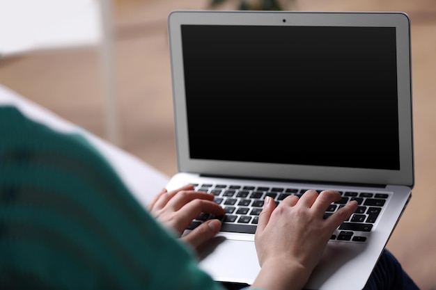 Mujer sentada en un sofá con una computadora portátil de rodillas en una habitación
