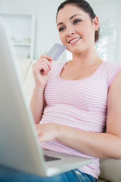 Mujer sentada en un sofá con una computadora portátil y una tarjeta de crédito