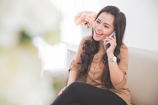 Mujer sentada en un sofá, llamando amigo con teléfono inteligente