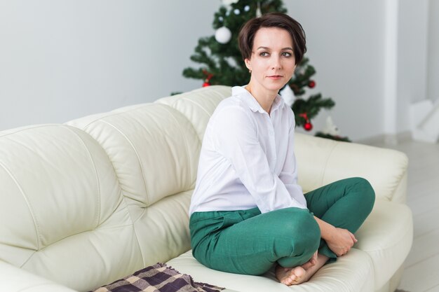 Mujer sentada en un sofá en la sala de estar con árbol de navidad