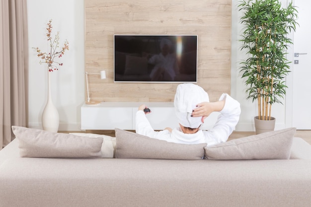 Mujer sentada en un sofá con una toalla sobre su cabeza viendo televisión