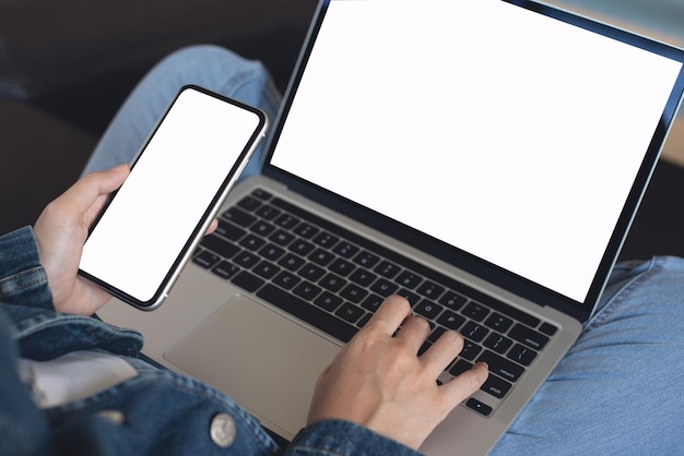 Mujer sentada en un sofá usando un teléfono móvil con pantalla en blanco y una computadora portátil en casa