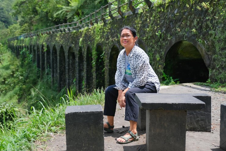 Foto mujer sentada sola en un bloque de hormigón disfrutando del día soleado en el puente plunyon kaliurang