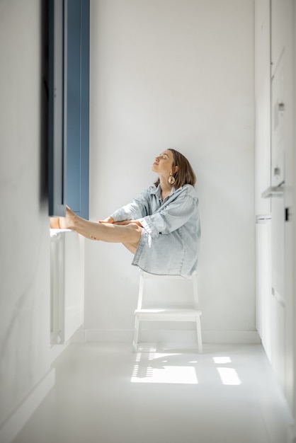 Mujer sentada sola junto a la ventana en casa