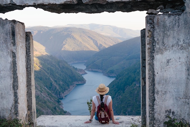 Mujer sentada con sombrero y mochila mirando el paisaje de montañas y ríos Copiar espacio Paicega Pesoz