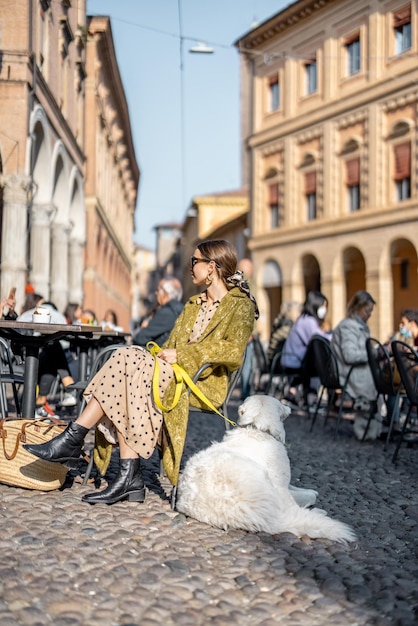 Mujer sentada con su perro blanco en un café al aire libre en el casco antiguo de la ciudad de Bolonia