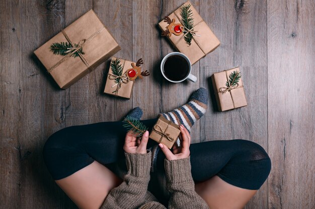 Una mujer sentada en el suelo envolviendo regalos y tomando café en Navidad