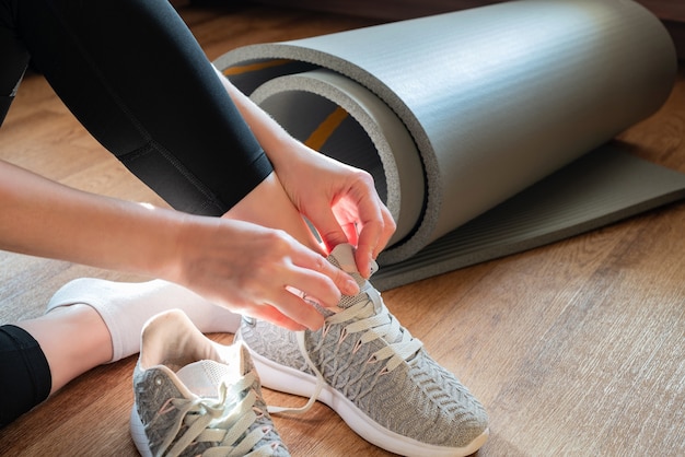 Mujer sentada en el suelo junto a la alfombra retorcida y atar sus zapatillas de deporte preparándose para la clase de yoga