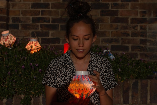 Mujer sentada en el suelo sosteniendo una linterna de papel rodeada de varios farolillos celebrando el día de las velas en Colombia