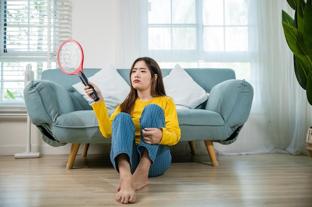 mujer sentada en el suelo usando un matador de mosquitos o una raqueta eléctrica