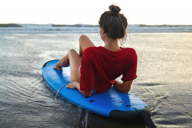 Mujer sentada en una tabla de surf en la playa después de su sesión de surf