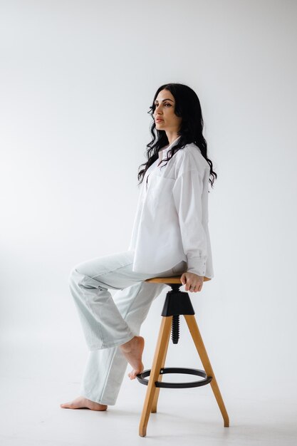 mujer sentada en un taburete con camisa blanca y pantalones con una almohada negra en la espalda foto gratis