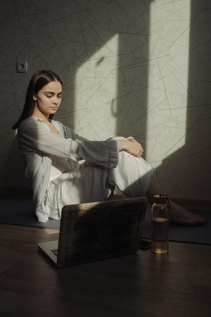 mujer sentada en un tatami y practicando yoga mientras ve una lección en línea