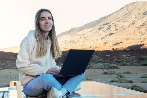 Mujer sentada en el techo de una furgoneta usando una computadora portátil