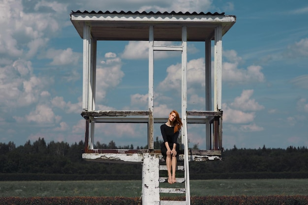 Mujer sentada en la torre de observación en el campo contra el cielo