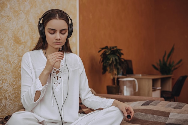 Mujer serena en auriculares escuchando música y haciendo aromaterapia con aceite esencial