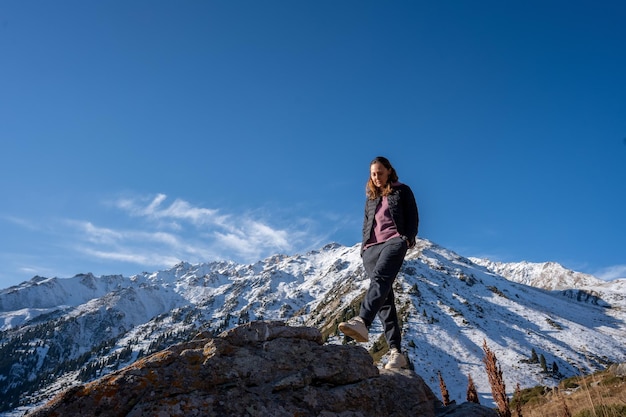 Mujer serena caminando sobre una roca paseando rodeada de montañas nevadas