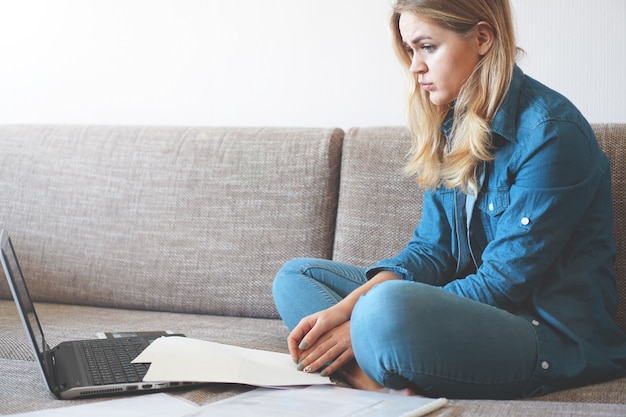 Mujer seria centrada en buscar información. Sentado en casa frente a una computadora portátil. El concepto de negocios y aprendizaje de estudiantes en línea.