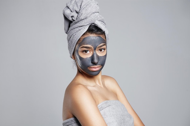Mujer seria haciendo tratamiento facial mascarilla gris facial de arcilla