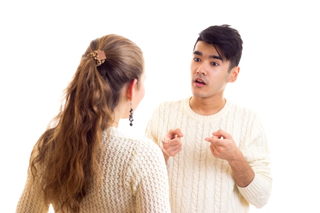 Mujer seria joven con hombre joven con cabello oscuro en suéteres blancos y jeans hablando en estudio