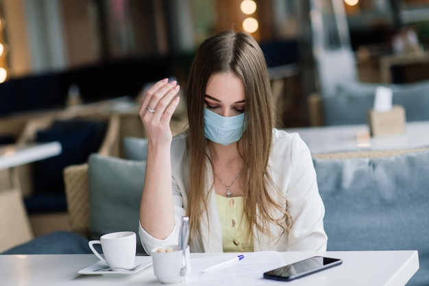 Mujer seria con mascarilla protectora comprobación de noticias en la terraza de un café