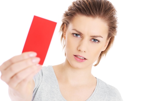 Una mujer seria mostrando una tarjeta roja sobre fondo blanco.