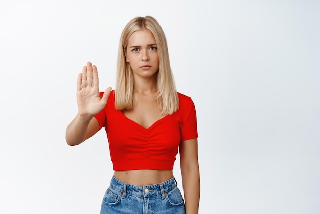 Una mujer seria parece preocupada y muestra un gesto de prohibición de dejar de decir que no se desaprueba algo sobre fondo blanco.