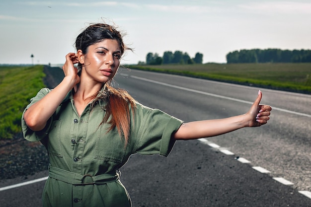 Una mujer sexy y adorable con un mono ajustado está tratando de atrapar un auto en la carretera, retrato