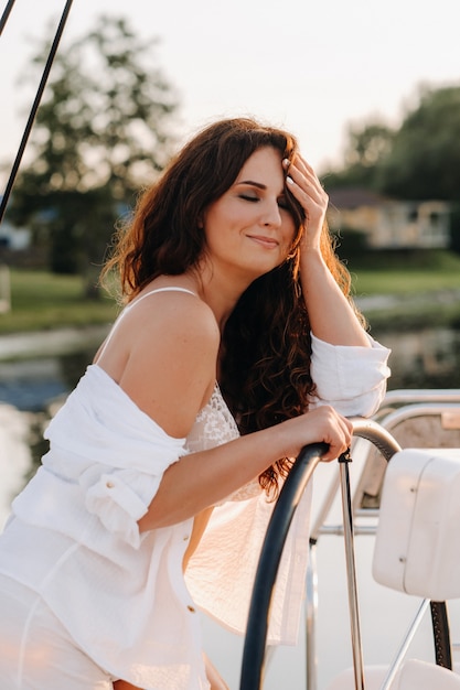 Mujer sexy con una camisa blanca disfruta de la puesta de sol en su yate blanco privado