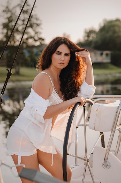 Mujer sexy con una camisa blanca disfruta de la puesta de sol en su yate blanco privado