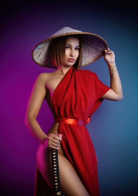 La mujer sexy con una capa roja y un sombrero asiático con una katana en la mano imagen de un samurai en color neón