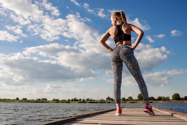 Mujer sexy deportiva en ropa deportiva en el muelle en el fondo del agua