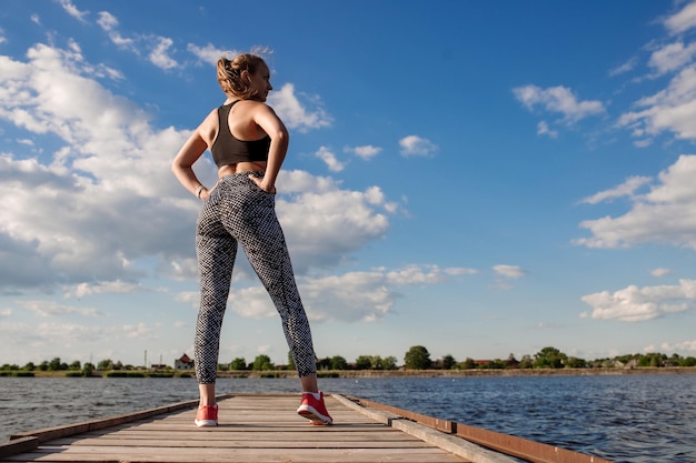 Mujer sexy deportiva en ropa deportiva en el muelle en el fondo del agua