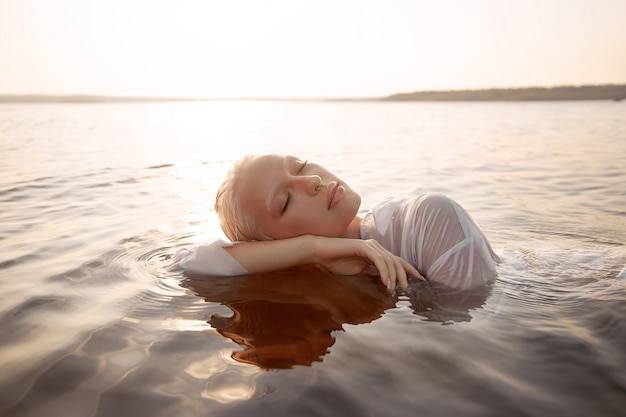 Mujer sexy desnuda desnuda en el agua al atardecer. Hermosa mujer rubia con pelo corto mojado y pechos grandes, retrato de arte en el mar