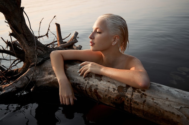 Mujer sexy desnuda desnuda en el agua al atardecer. Hermosa mujer rubia con pelo corto mojado y pechos grandes, retrato de arte en el mar