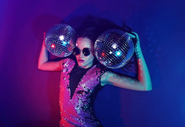 Foto mujer sexy fiesta disco. gafas de sol, vestido de fiesta de lentejuelas, bolas de discoteca, luces de neón, maquillaje brillante.