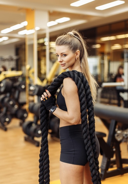 Mujer sexy en forma posando con cuerdas de batalla en el gimnasio