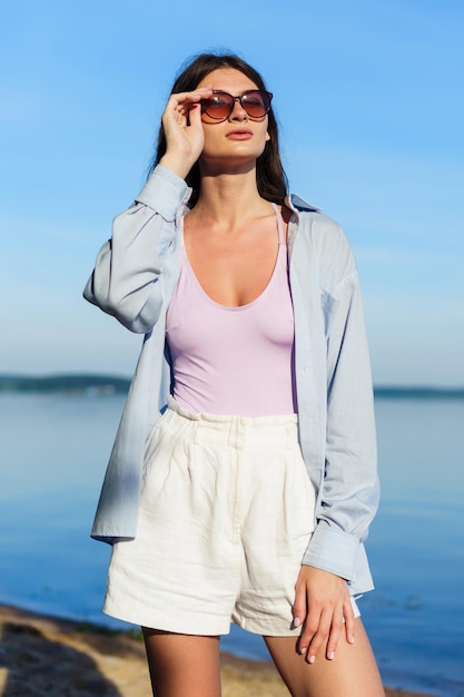 Mujer sexy joven en camisa y pantalones cortos posando en la playa