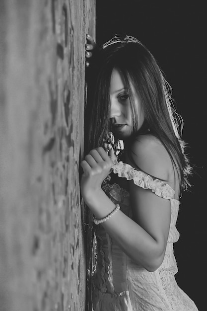 Mujer sexy joven desnuda contra la pared con textura vintage. Linda chica en corsé francés blanco sin ropa interior. Actriz esbelta desnuda muestra emociones en la sesión de fotos. Contenido para adultos con parte del cuerpo desnudo