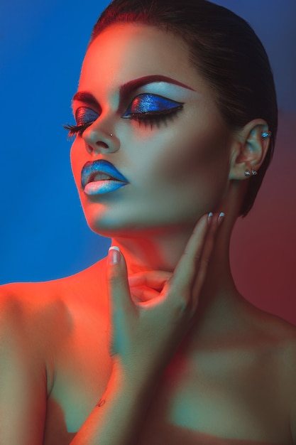 Mujer sexy con maquillaje y ojos cerrados en luces rojas y azules en estudio