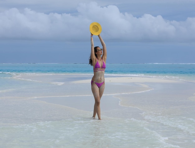 mujer sexy en un sombrero de paja se encuentra en la arena del mar