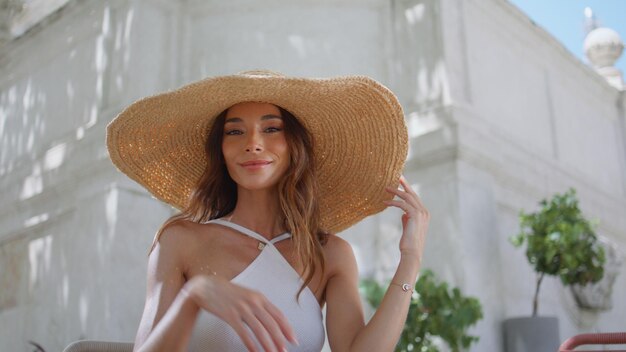 Mujer sexy tocando un sombrero de paja posando con una sonrisa suave en el retrato de un café a la luz del sol