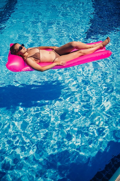 Foto mujer sexy en traje de baño se encuentra en un colchón inflable rosa en la piscina relájese junto a la piscina en un caluroso día soleado de verano concepto de vacaciones