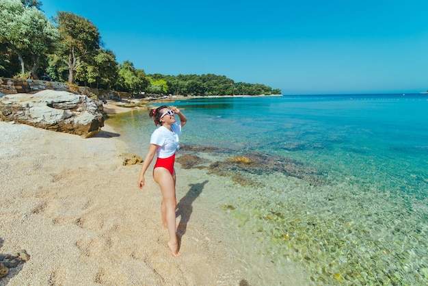 Mujer sexy en traje de baño rojo y camiseta blanca en la playa del mar