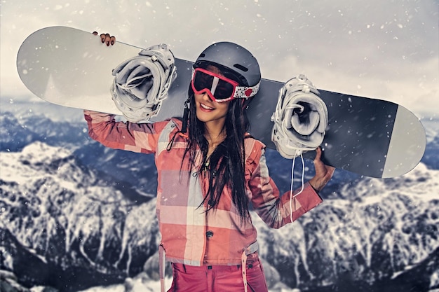 Mujer sexy en traje de esquí posando con snowboard en un estudio sobre fondo gris.