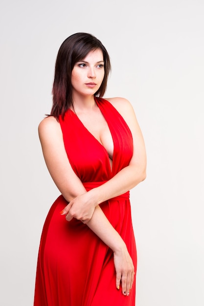 Mujer sexy en vestido rojo con escote profundo en pared gris