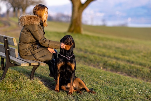 Una mujer se sienta en un banco y abraza a un rottweiler en una colina por la mañana