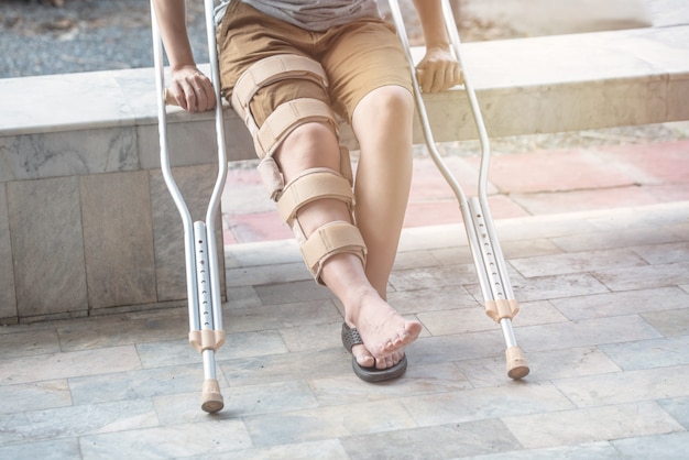 Foto la mujer se sienta en el banco con bastón y soporte de rodilla cirugía de soporte rodilla derecha en tiempo de recuperación.