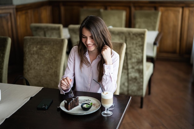 la mujer se sienta en la cafetería del restaurante del café en el interior y come pastel de postre de brownie de chocolate