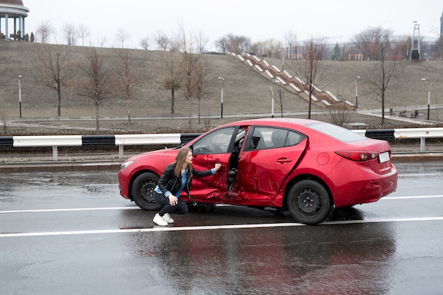 La mujer se sienta cerca de un coche averiado después de un accidente. llamar por ayuda. seguro de auto